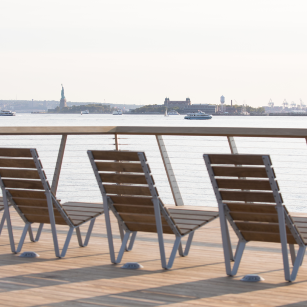 A row of chairs looking over the Hudson River face a sunny view of the Statue of Liberty from Hudson River Park's Pier 26